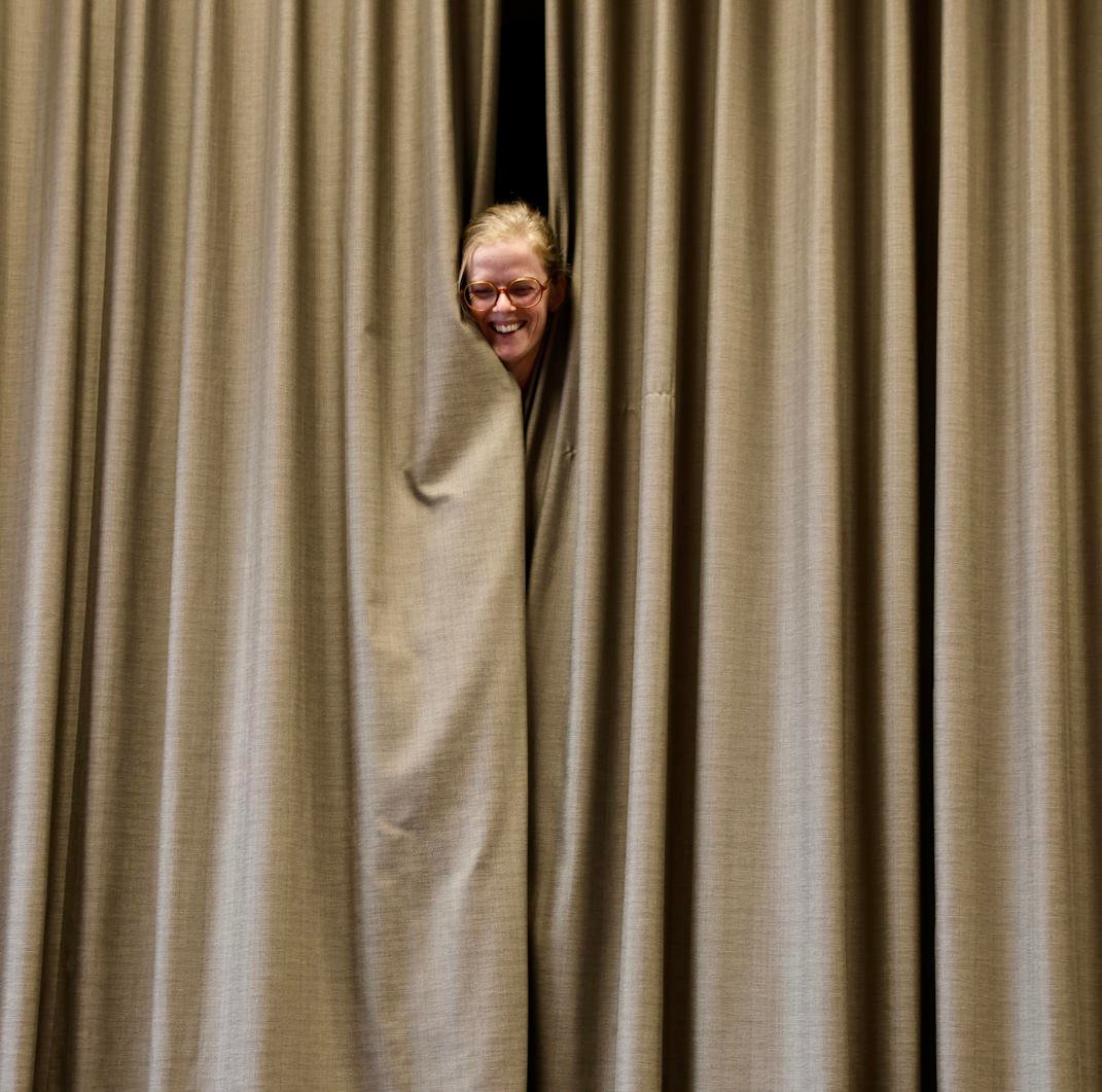 Improvisatiespeler gluurt speels tussen theatergordijnen tijdens open repetitie van Improfiel.
